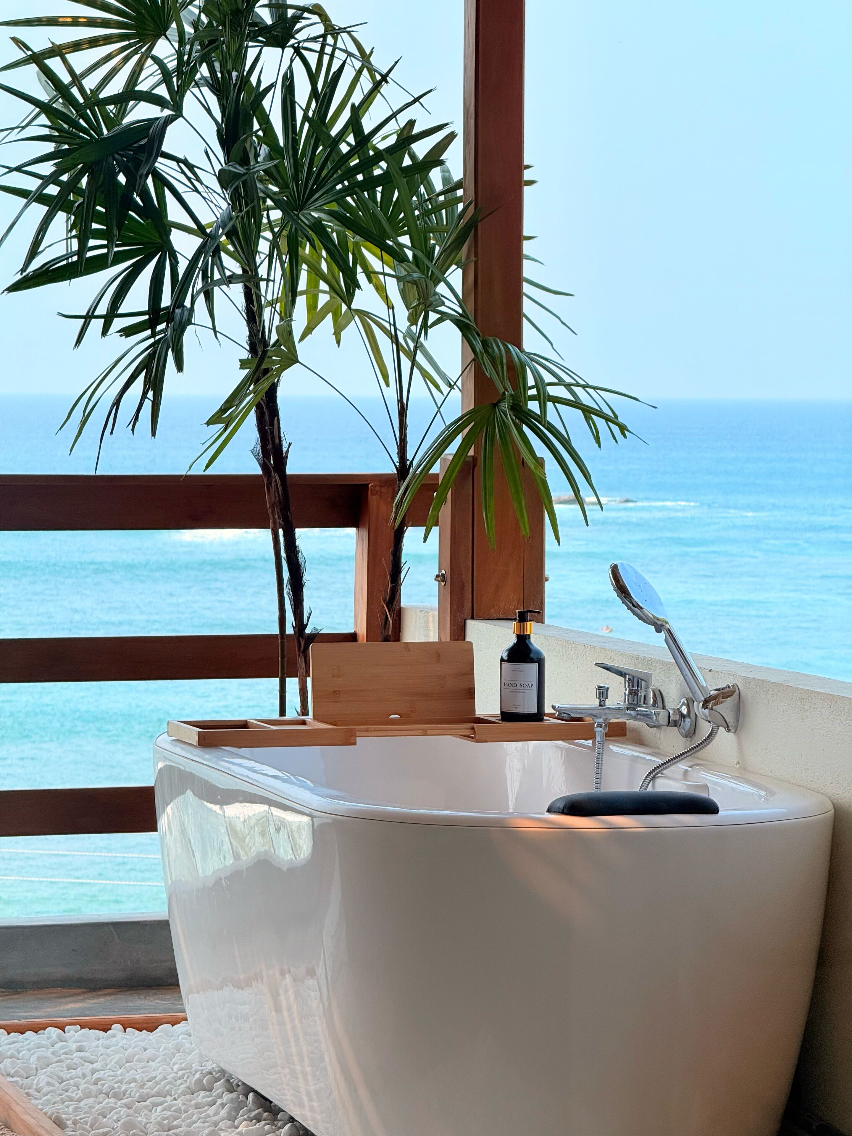 A bathroom with a bathtub, wooden bench, and a bottle of hand soap.