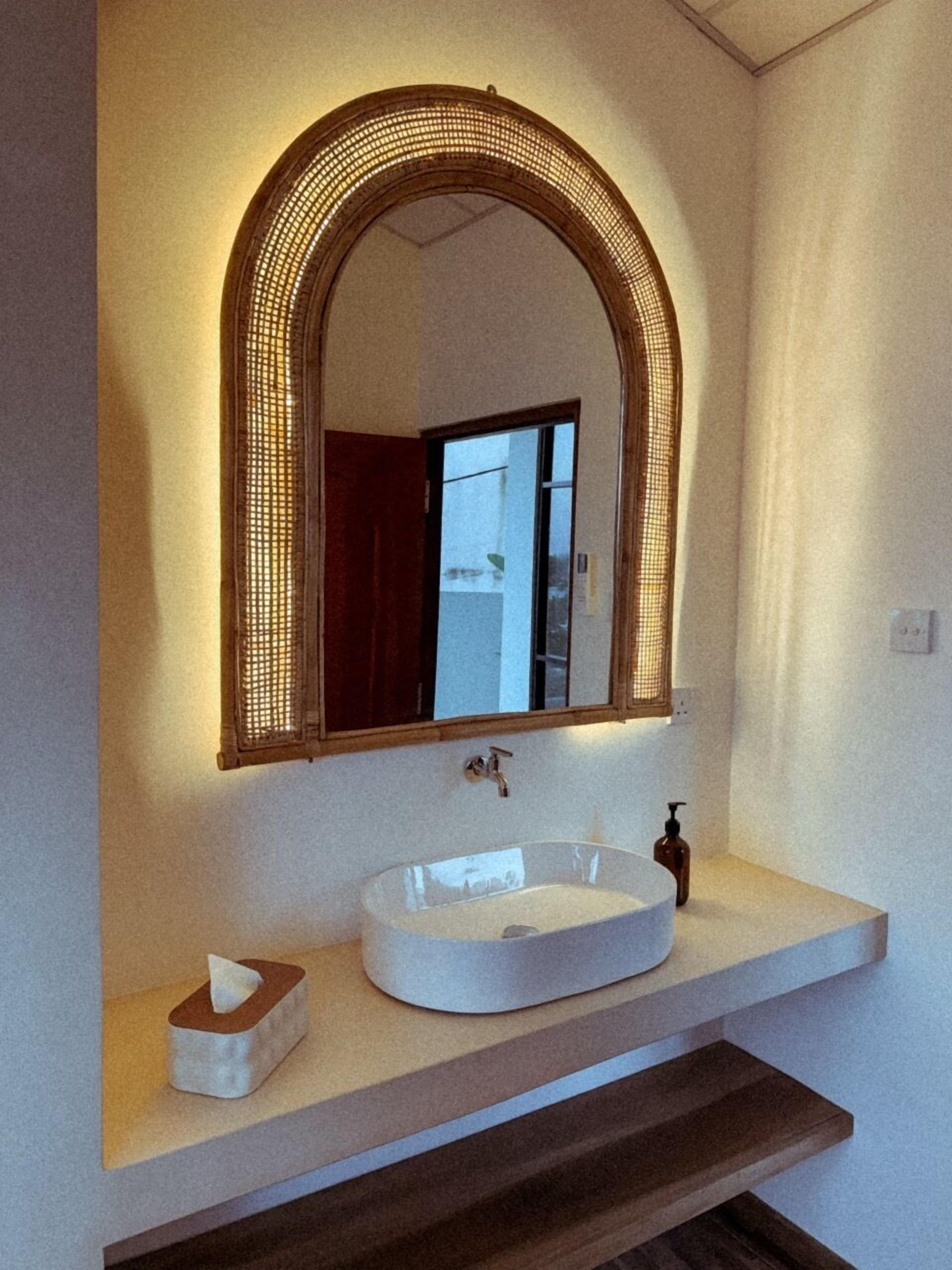 Un baño con un lavabo blanco, un espejo de marco arqueado y una caja de pañuelos en la encimera.