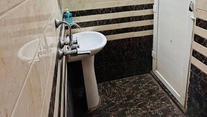 A small, narrow bathroom with a toilet, sink, and a red bucket on the floor. - Maya Inn Paying Guest House By GRB (Varanasi)