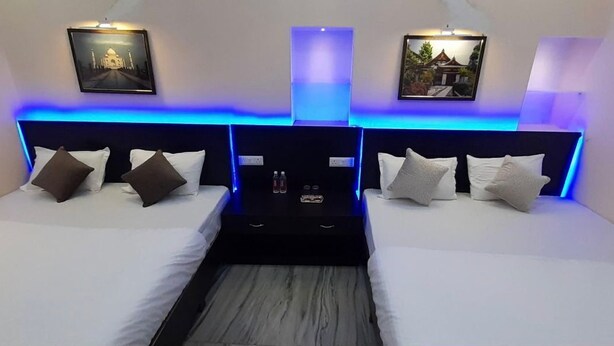 A modern hotel room with two beds, each with a headboard, white bedding, and a central table with amenities. - Maya Inn Paying Guest House By GRB (Varanasi)
