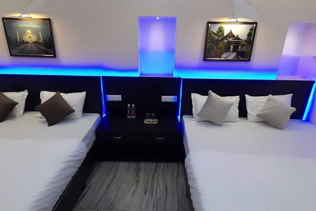 Ein modernes Hotelzimmer mit zwei Betten, jeweils mit Kopfteil, weißer Bettwäsche und einem zentralen Tisch mit Annehmlichkeiten.