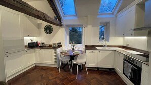 Una cocina moderna con armarios blancos, suelo de madera en espiga, una mesa redonda y dos tragaluces.