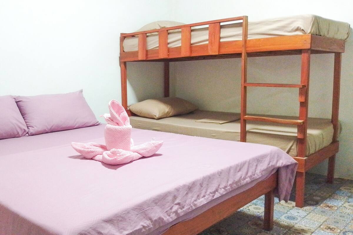 Una cama individual con una colcha morada y una toalla rosa.
