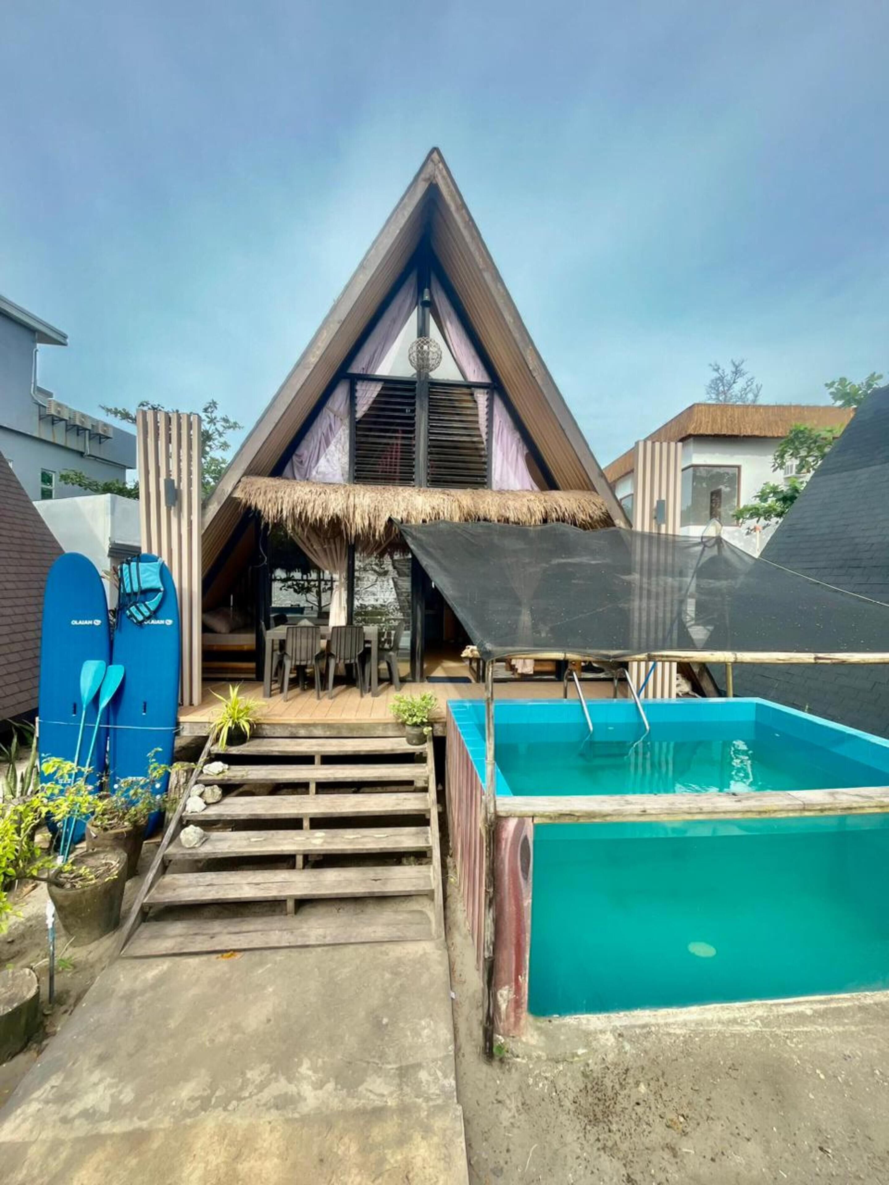 A triangular building with a thatched roof, a pool, and a surfboard rack.