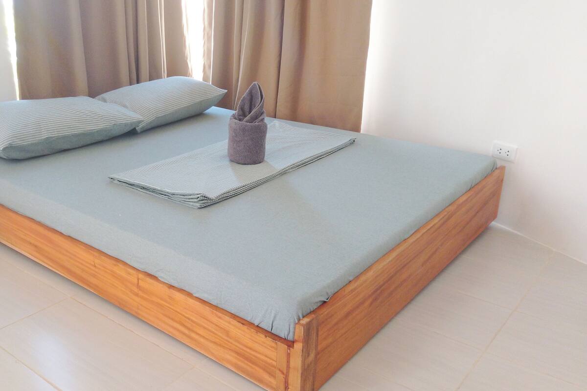 Una cama bien hecha con un colchón gris, dos almohadas y una toalla doblada.
