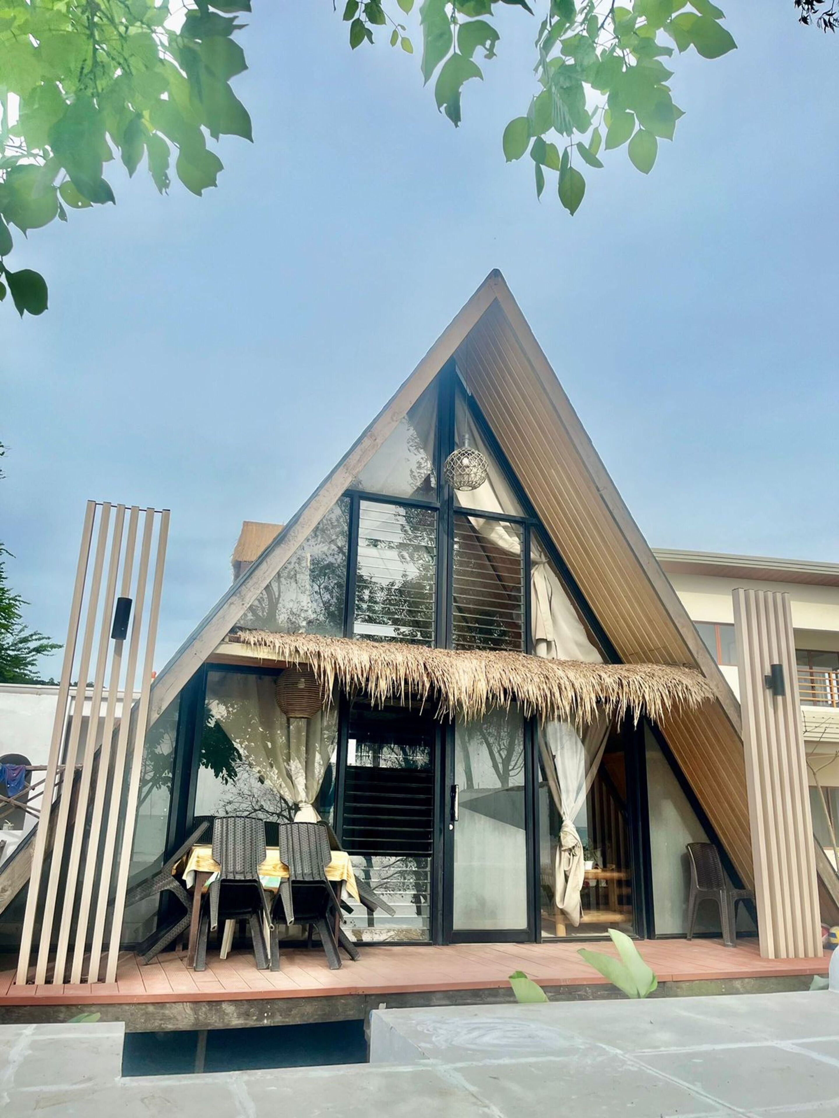 A modern building with a triangular roof, large glass windows, and a thatched roof entrance.