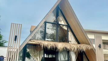 A modern building with a triangular roof, large glass windows, and a thatched roof entrance.