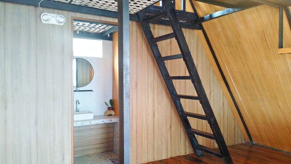 A room with a wooden floor, a black ladder, a white sink, and a mirror.