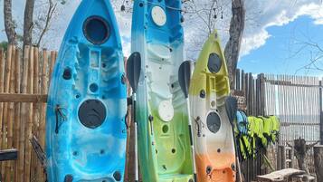 Tres kayaks alineados en una playa arenosa, con una valla de madera y árboles al fondo.