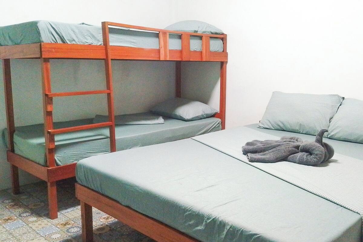 Una habitación con dos literas y una cama individual, cada una con almohadas y mantas.