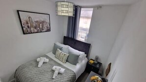 A bedroom with a bed, pillows, a bedside table, a lamp, and a painting on the wall. - FC Platinum Accommodation (Watford)