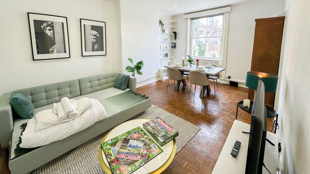 Un salon moderne comprenant un canap é, une table basse avec un jeu de société, un coin repas avec une table et des chaises, et un téléviseur.