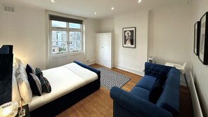 Une chambre moderne avec un lit, un canapé bleu, un tapis à motifs et une fenêtre donnant sur des immeubles.