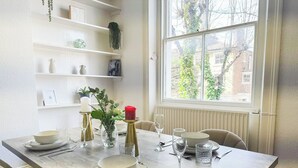 Un coin repas avec une table dressée pour quatre personnes, entouré d’étagères blanches ornées d’objets décoratifs.