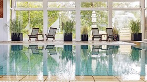 An indoor swimming pool with clear glass walls, surrounded by potted plants and wicker chairs. - 6 Person Holiday Home in Gilleleje (Gilleleje)