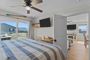Une chambre avec un grand lit, un ventilateur de plafond, une télévision et une vue sur le jardin arrière.