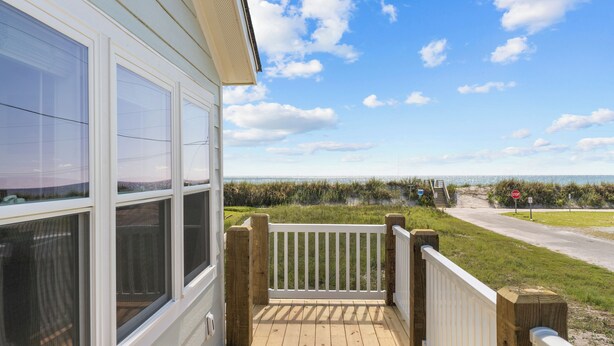 Una terraza de madera con barandilla blanca, con vista a una playa y una señal de stop.
