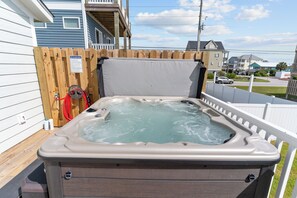 Un bain à remous avec une terrasse en bois et une clôture blanche, entouré de maisons et sous un ciel dégagé.