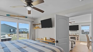 Un dormitorio con una cama grande, ventilador de techo, televisor y vista al jardín trasero.