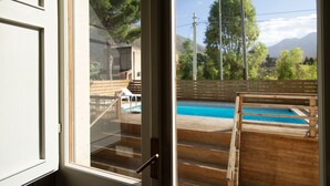 A view through a window of a wooden deck with a pool, steps, and a clear sky.