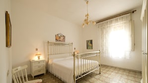 A bedroom with a bed, a nightstand, a chair, and a window with curtains.