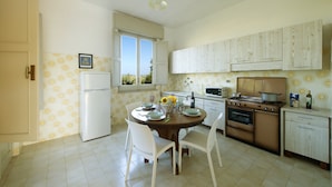 A kitchen with a dining table, chairs, a refrigerator, a stove, and cabinets.