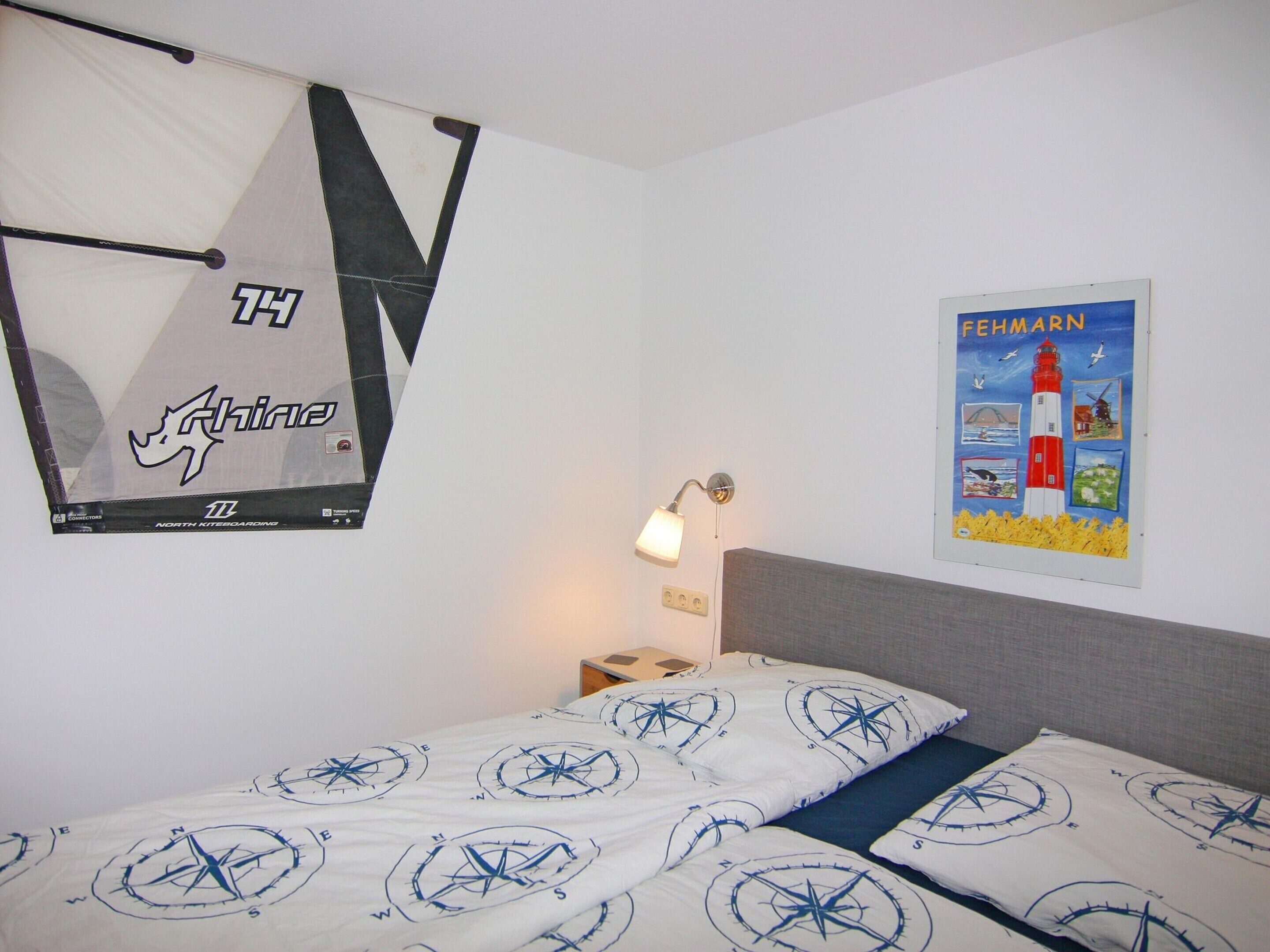 Hotellihuone, jossa on kompassikuviolla varustettu sänky, seinälle kiinnitetty kartta ja majakan kuva.