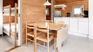 A compact wooden cabin with bunk beds, a dining area with a table and chairs, a kitchenette, and a hanging light fixture. - Stunning Cabin in Camping Resort (Lokken)