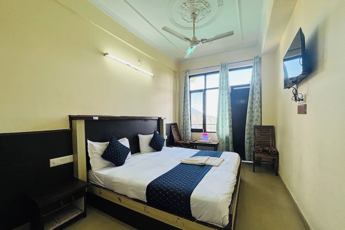 A hotel room with a bed, a desk, a chair, a television, and a window with curtains.