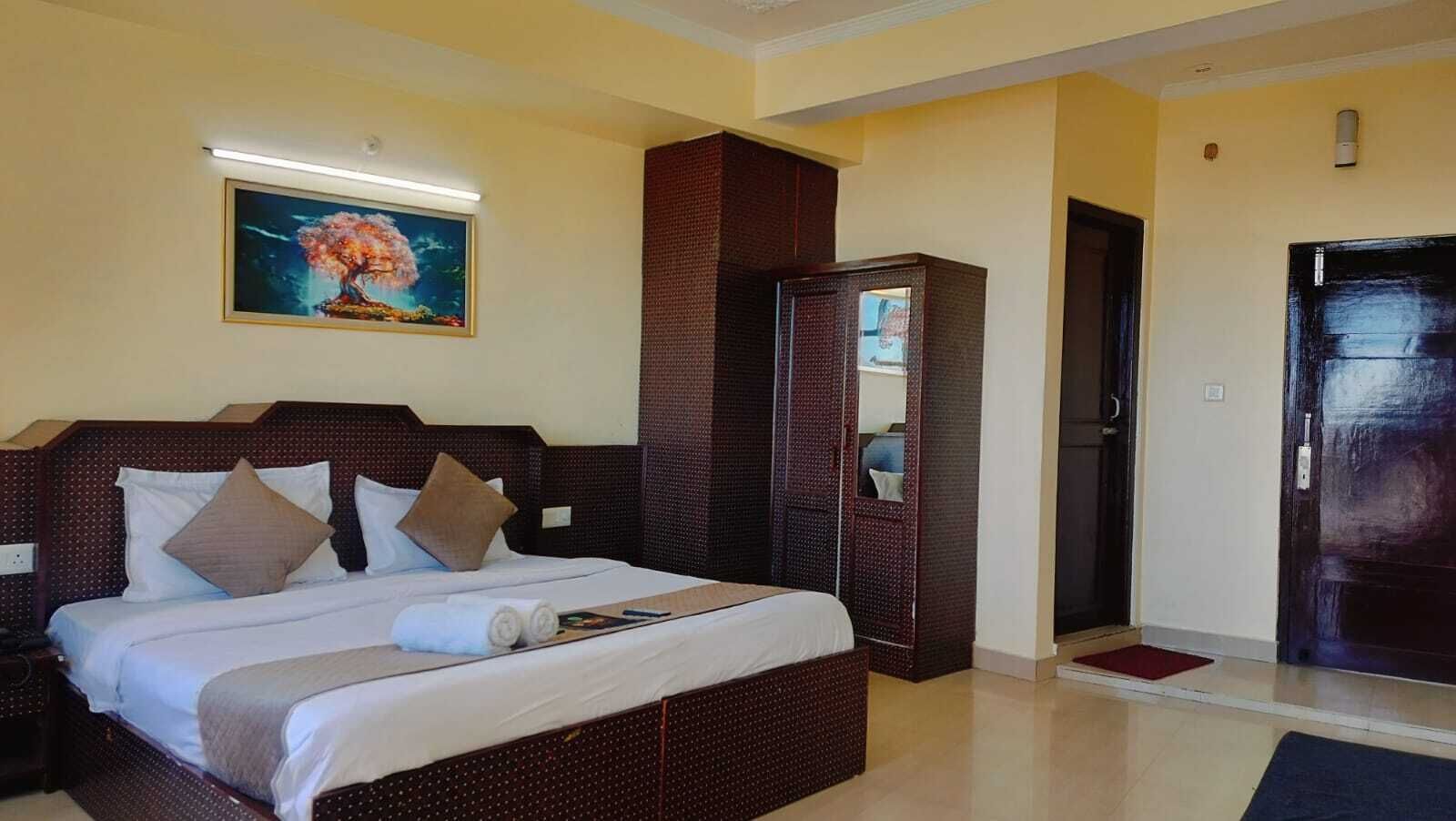 A hotel room with a large bed, a wardrobe, and a painting on the wall.