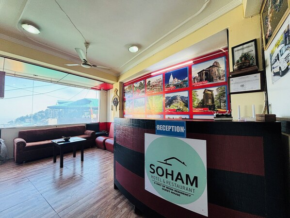 Un espace d’accueil avec une enseigne indiquant « SOHAM HOTEL & RESTAURANT » et un mur recouvert de tableaux encadrés.