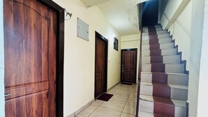 Un pasillo con puertas de madera, piso de baldosas y una escalera con peldaños rojos y blancos alternados.