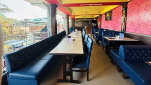 Un restaurante con cabinas y mesas, techo rojo y amarillo, y vista al exterior.