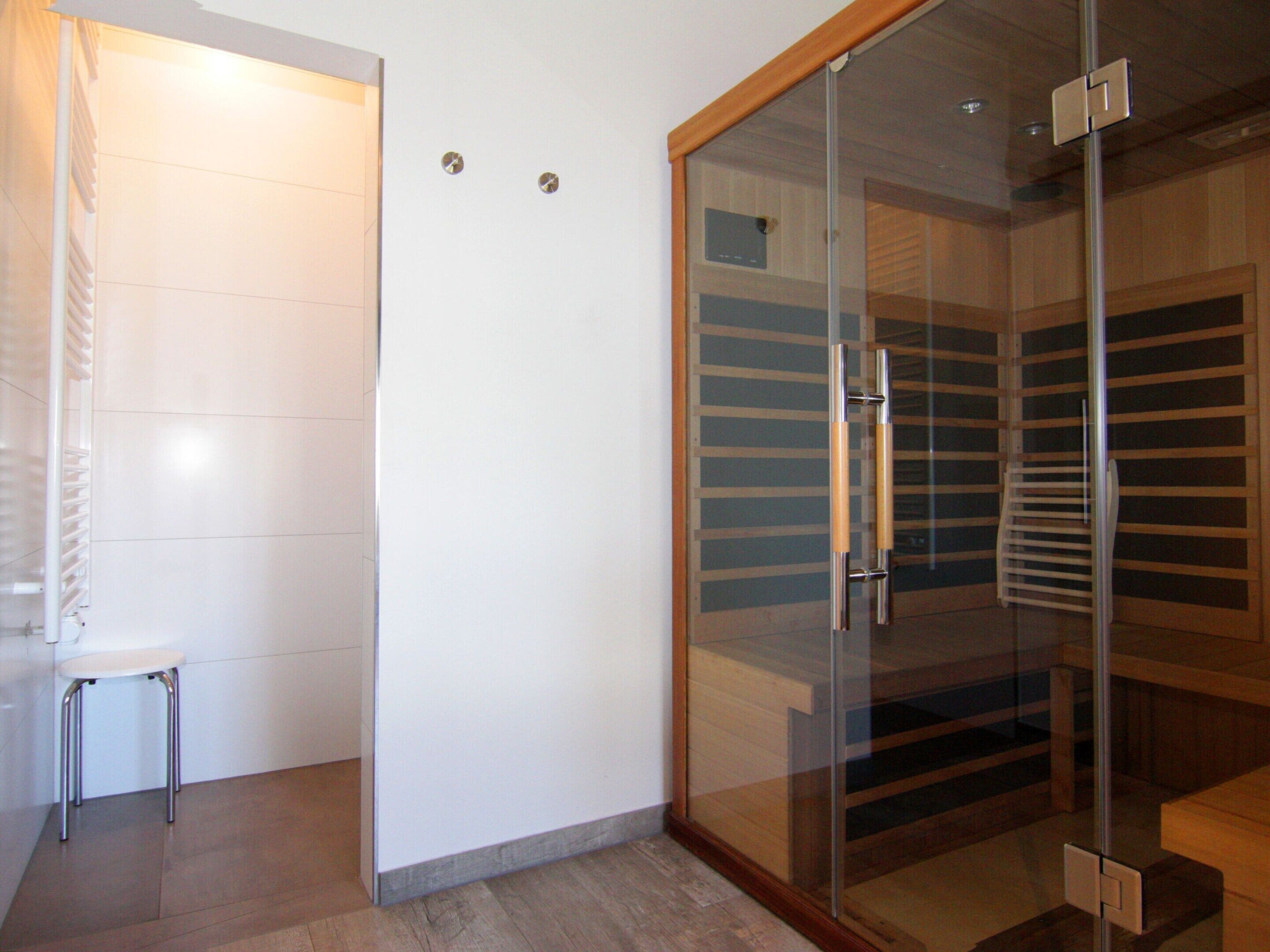 A modern bathroom with a glass shower enclosure, a white toilet, and a small stool.