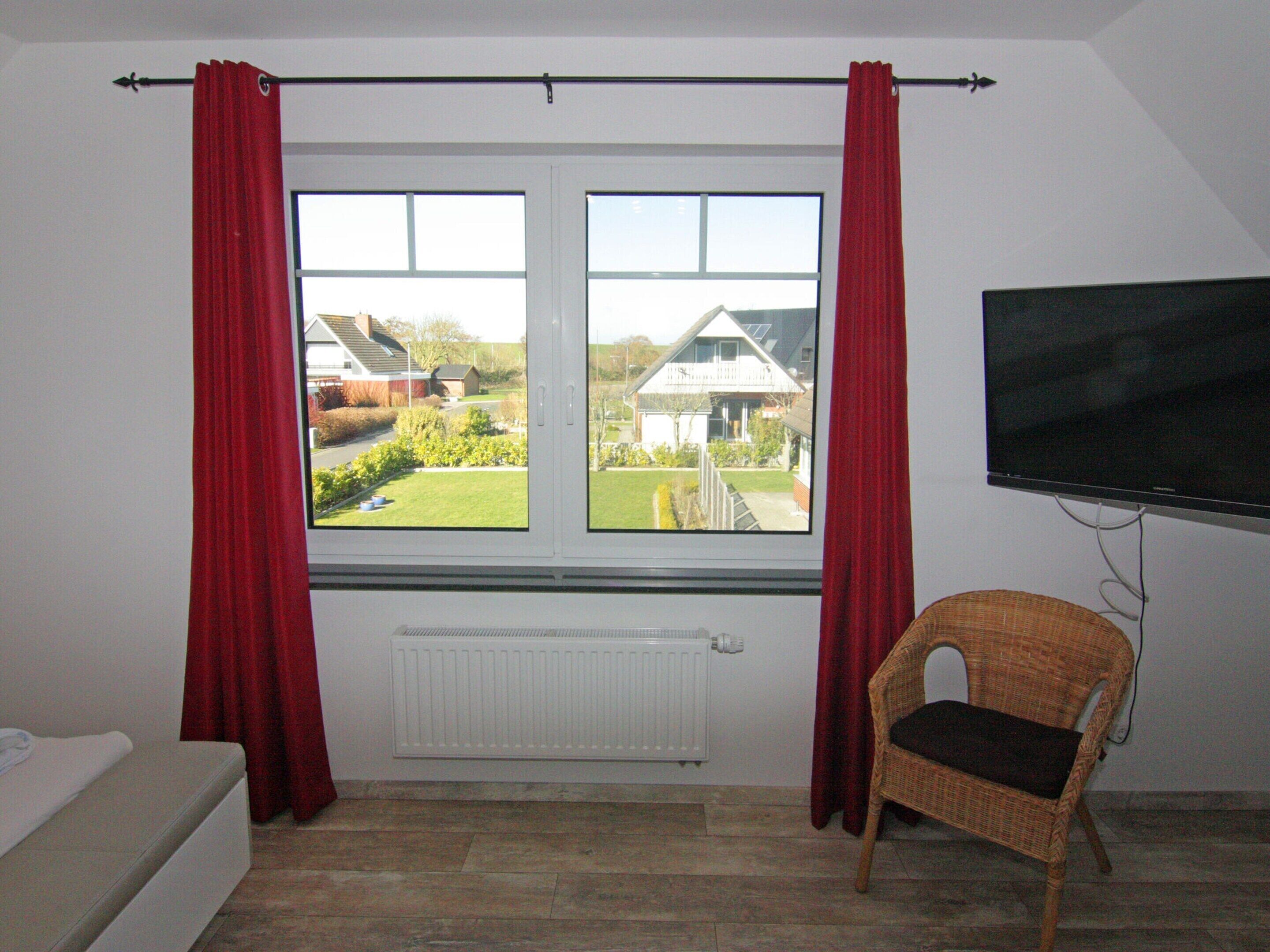 A room with a bed, a chair, a TV, and a window with curtains.