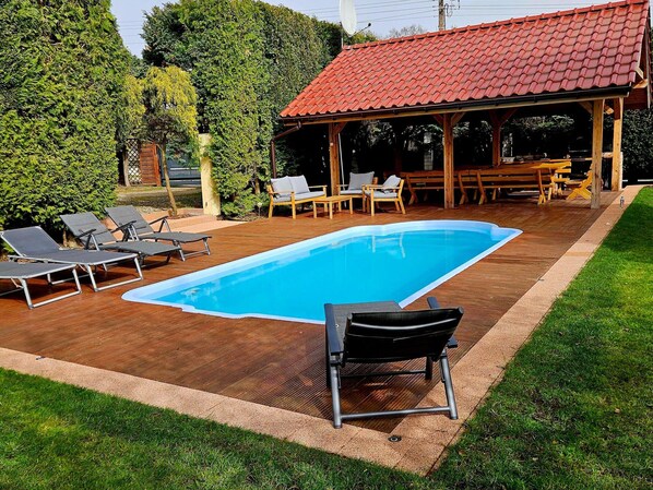 Relax by the pool surrounded by lush greenery and a wooden pergola.