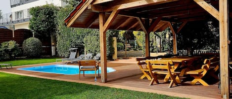 A covered outdoor area with a pool, lounge chairs, and a wooden table.