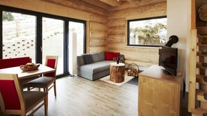 Interior acogedor de una cabaña con techo de madera, un sofá, una mesa de comedor con sillas y un televisor.