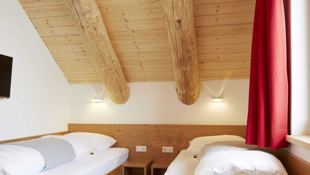 A room with two wooden beds, a small wooden table, and a red curtain. - Chalet in Ladis by Ski Slope & Sonnenbahn (Ladis)
