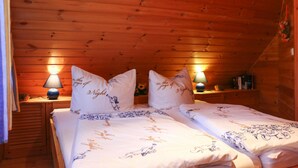 Een gezellig houten kamer met slaapkamer, met twee bedden, elk voorzien van passende kussens en een bloemenbedekking. Er staan twee bedlampen op houten nachtkastjes.