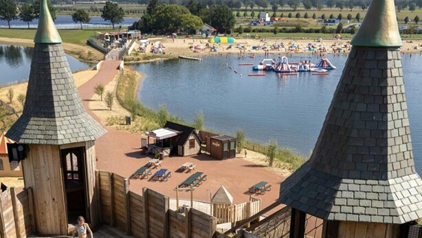 A lakeside view with two prominent conical structures, a sandy beach area with lounge chairs, and a small building with a red roof. - Pet Friendly & Peaceful Stay (Beesel)
