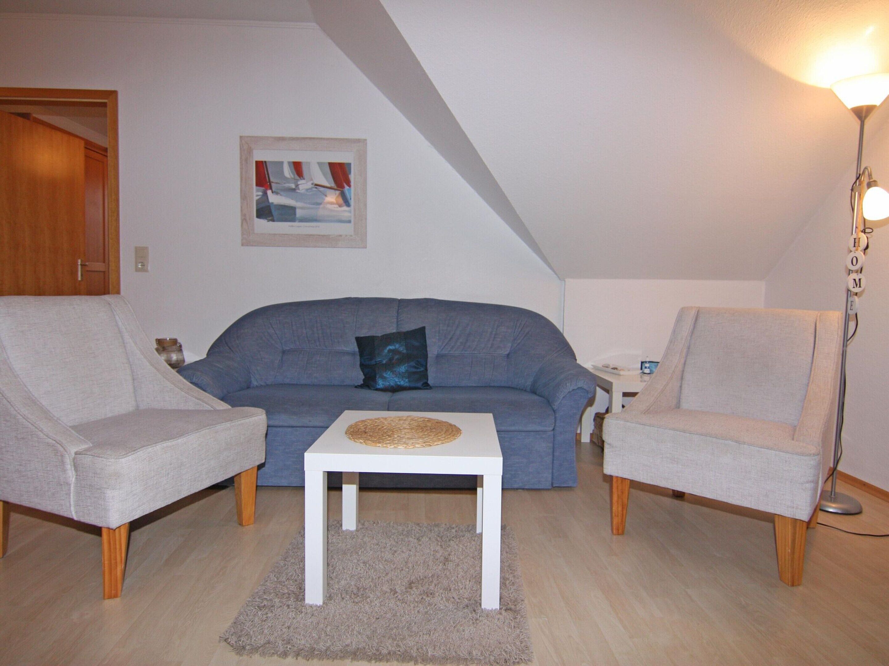 A living room with a blue sofa, two grey armchairs, a white coffee table, and a lamp.