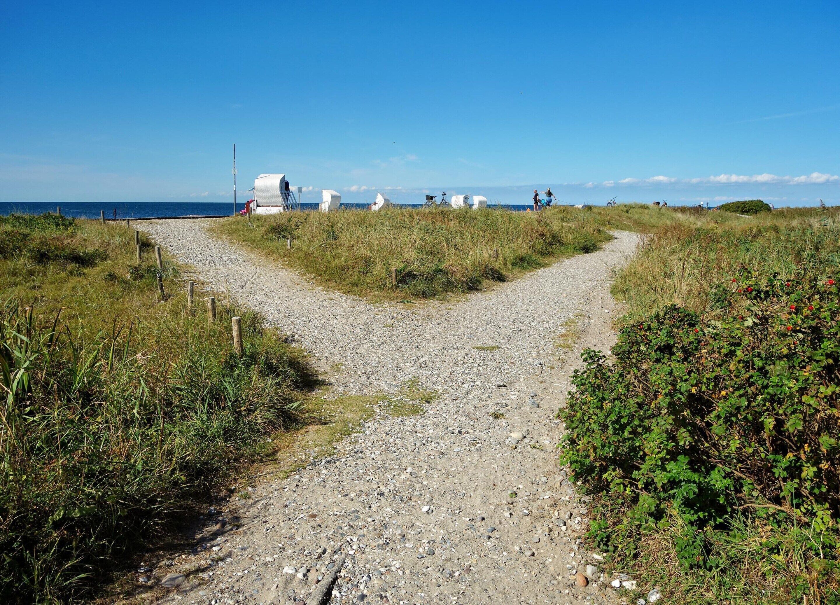 A gravel path leading to a beach with white structures and a clear blue sky.