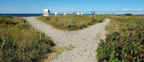 A gravel path leading to a beach with white structures and a clear blue sky.