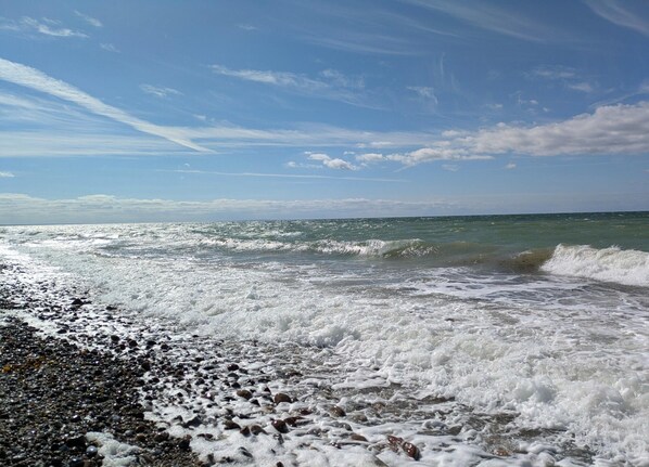 Une plage où les vagues se brisent sur un rivage de galets, sous un ciel dégagé.