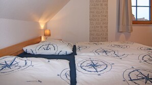 Une chambre à coucher avec un lit orné d’un motif en forme de boussole, une lampe de chevet et une fenêtre donnant sur l’extérieur.