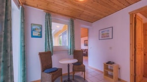 Een gezellige kamer met een houten plafond, twee rieten stoelen, een klein rond tafeltje en een raam met gordijnen.