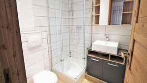 A modern bathroom with a glass shower enclosure, a white toilet, and a vanity with a sink and cabinets. - Skandinavisches Ferienhaus in Mirow (Mirow)
