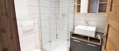 A modern bathroom with a glass shower enclosure, a white toilet, and a vanity with a sink and cabinets.