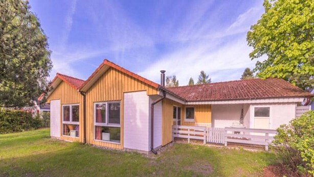 A two-story house with a red-tiled roof, a fenced yard, and a grassy front lawn. - Skandinavisches Ferienhaus in Mirow (Mirow)